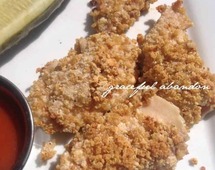 quinoa breaded chicken tenders that are Whole 30 and Paleo and gluten free on a white plate with dipping sauce and a pickle for garnish